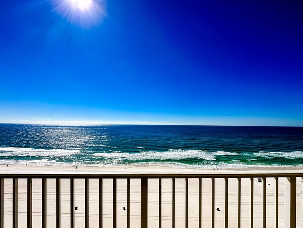 A beach with a wooden railing, clear blue sky, and calm ocean waves.