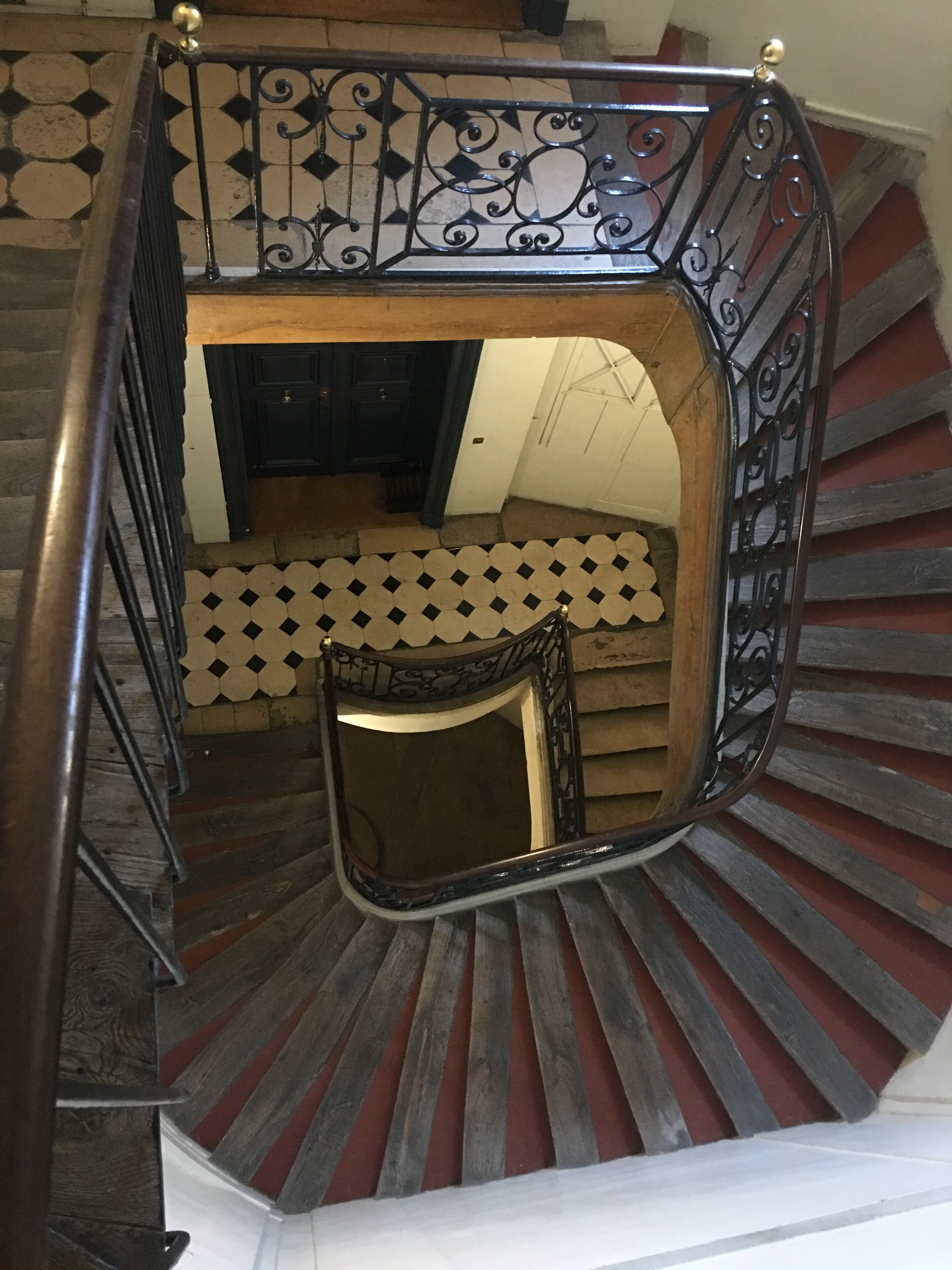 Una escalera de caracol con barandilla de metal negro y un suelo con estampado de cuadros.