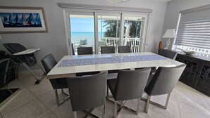 Un espace repas comprenant une grande table, des chaises et une vue sur l’océan, accessible par une porte-fenêtre coulissante.