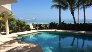 Une piscine aux eaux d’un bleu limpide, des chaises longues blanches et une vue sur l’océan.
