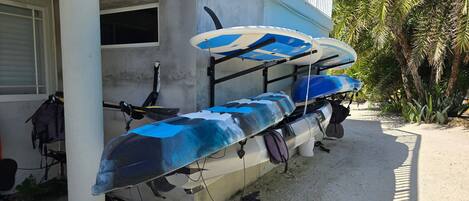 Des kayaks et une planche à pagaie sont appuyés contre un bâtiment dont la façade est en béton.