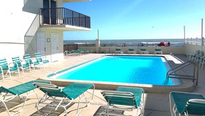 A pool area with a view of the ocean, a door, and several lounge chairs.