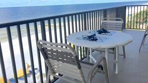 A balcony with a white table and chairs, overlooking the ocean.
