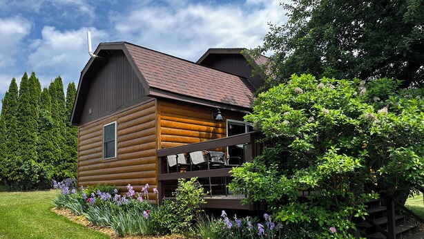 A log cabin with a deck and outdoor seating, surrounded by a well-maintained garden and tall trees. - Heritage hideaway-Secluded Log Cabin (Chatfield)