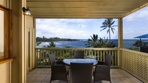 A balcony with a table and chairs overlooking a beach and ocean.