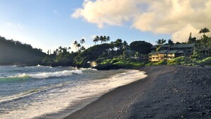 A beach with waves, a black sand shore, and a building with multiple floors and balconies.