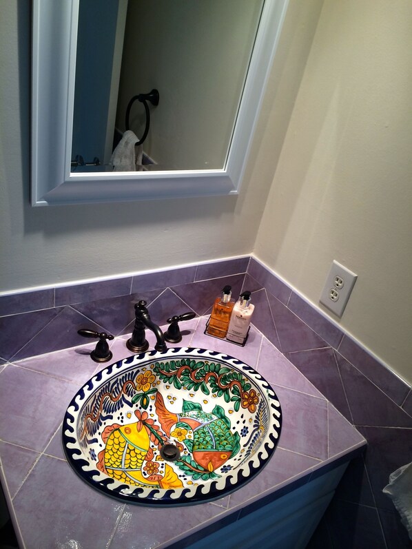 Un baño con un lavamanos decorativo, dos grifos y un espejo encima.