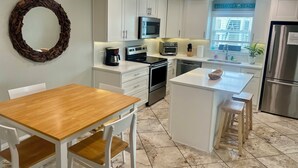 Una cocina moderna con armarios blancos, una mesa de comedor de madera, horno empotrado, microondas y refrigerador.