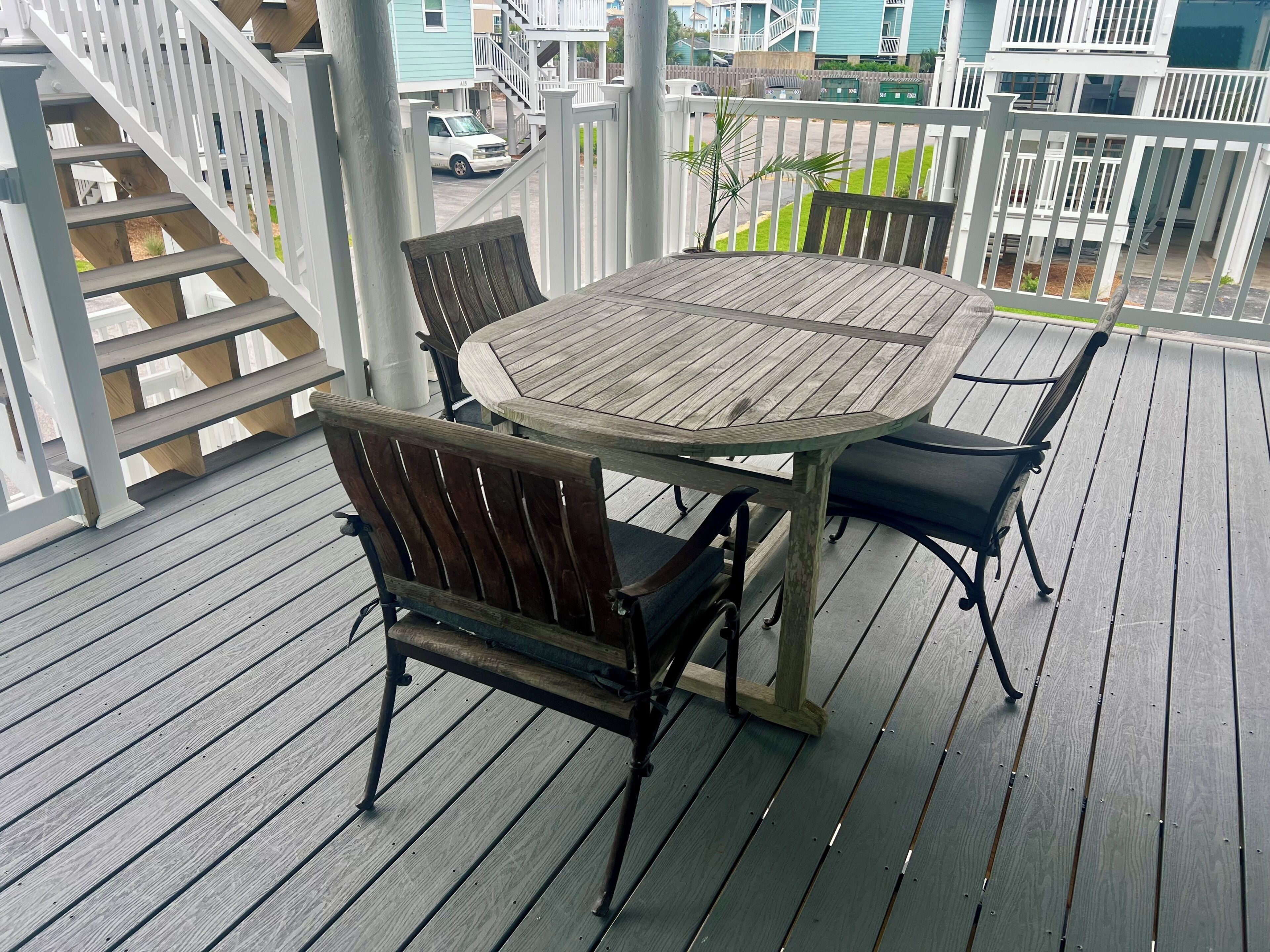 A wooden deck with a round table and chairs, a staircase, and a view of buildings in the background.