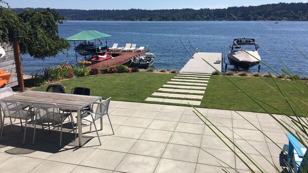 A patio with a table and chairs, a boat docked on the water, and a view of the lake and forested hills. - Waterfront & View-Near Seattle on Lake Sammamish in Bellevue (Bellevue)