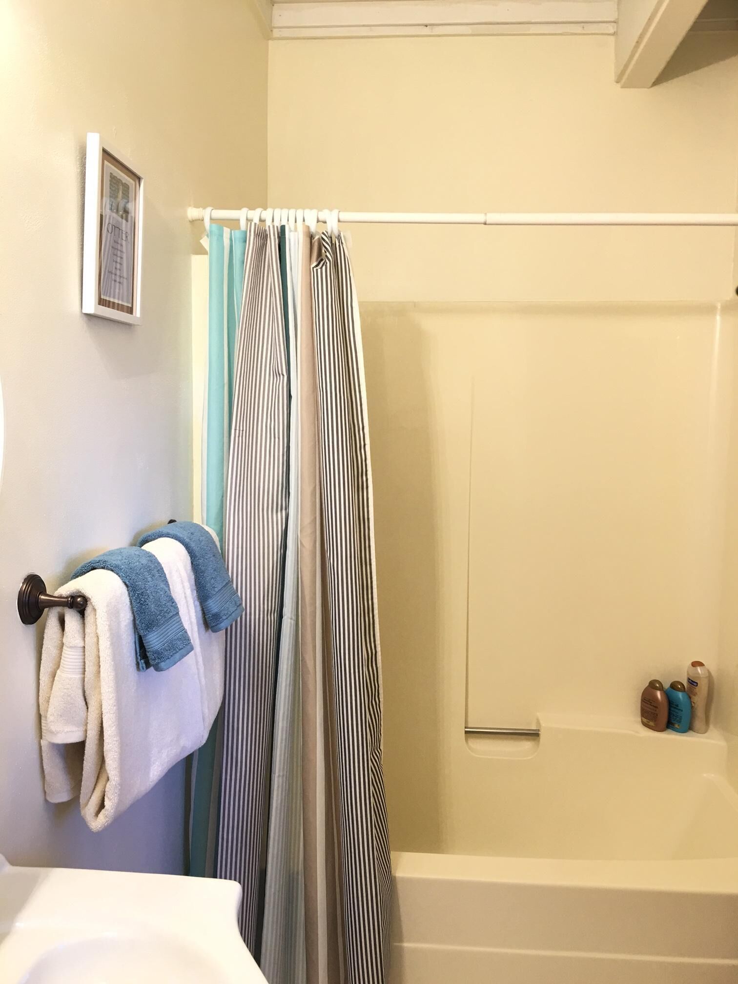 A bathroom with a bathtub, a towel rack with towels, a shower curtain, and toiletries on the wall.
