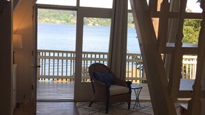 A room with a wooden floor, a wicker chair with a cushion, a small table, and a view of a lake through large windows. - Waterfront & View-Near Seattle on Lake Sammamish in Bellevue (Bellevue)