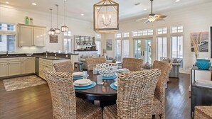 A spacious kitchen with modern appliances, a dining area with wicker chairs, and a large chandelier. - Perfect Family Getaway | Bikes, Courtyard w/Fire Feature, Walk to Pool & Fitness (Rosemary Beach)