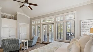 A bedroom with a bed, two chairs, a small table, a ceiling fan, and large windows with blinds. - Perfect Family Getaway | Bikes, Courtyard w/Fire Feature, Walk to Pool & Fitness (Rosemary Beach)