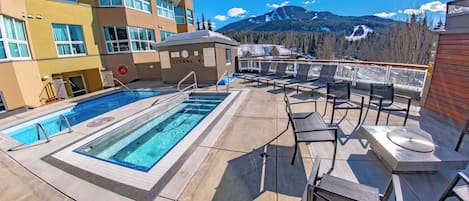 A rooftop pool area with a view of mountains, lounge chairs, and a lifebuoy.