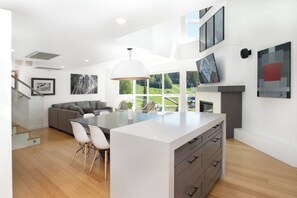 A modern kitchen with a central island, a dining area with chairs, a staircase, and artwork on the walls. - Le Chamois 510 - Upper Village (Whistler)