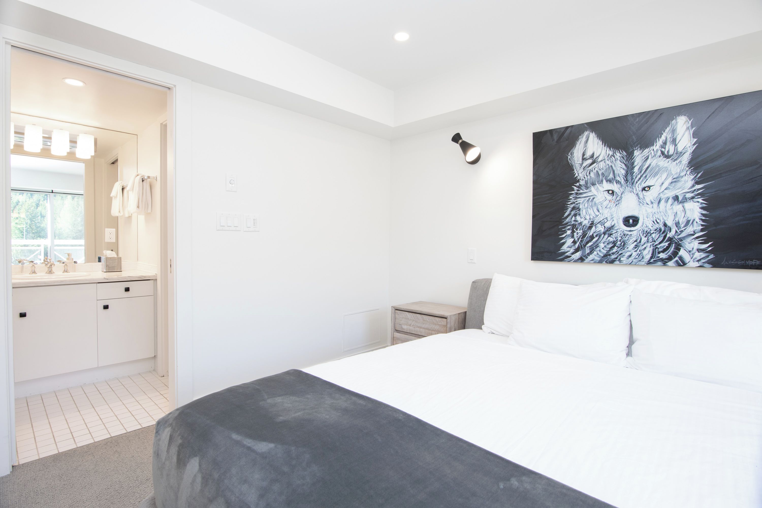 Un dormitorio moderno con una cama grande, una mesita de noche, una lámpara de pared y un cuadro de un lobo.