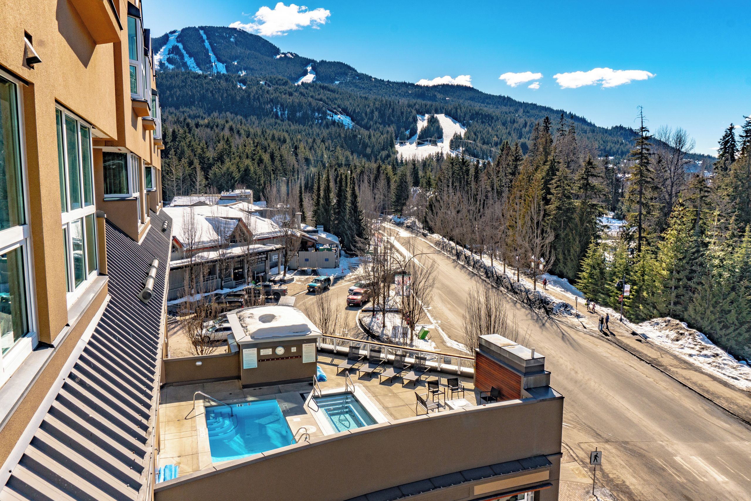 A hotel with a pool, ski slope view, and a road with snow.