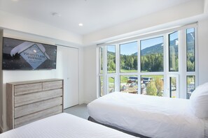 A hotel room with a large window, a bed, a wooden headboard, and a flat-screen TV mounted on the wall. - Le Chamois 510 - Upper Village (Whistler)