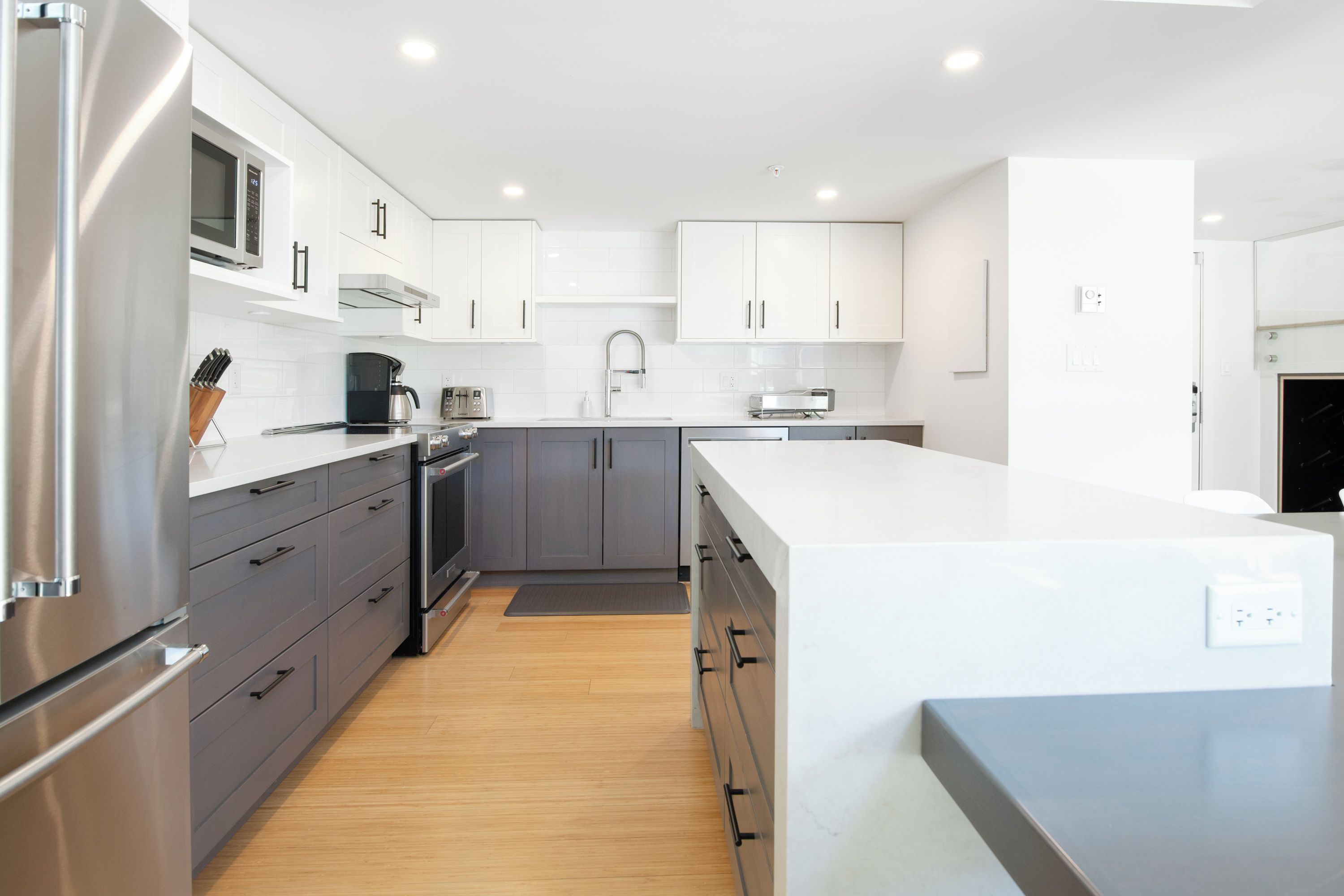 A modern kitchen with white cabinets, stainless steel appliances, and a wooden floor.