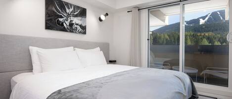 A modern hotel room with a large bed, a painting of a moose, a balcony with a mountain view, and a sliding glass door.
