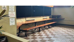 Ein Raum mit Holzbänken, einer Tafel und einem Fliesenboden.