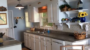 A kitchen with white cabinets, a wooden island, a hanging light fixture, and a window with a view of greenery.