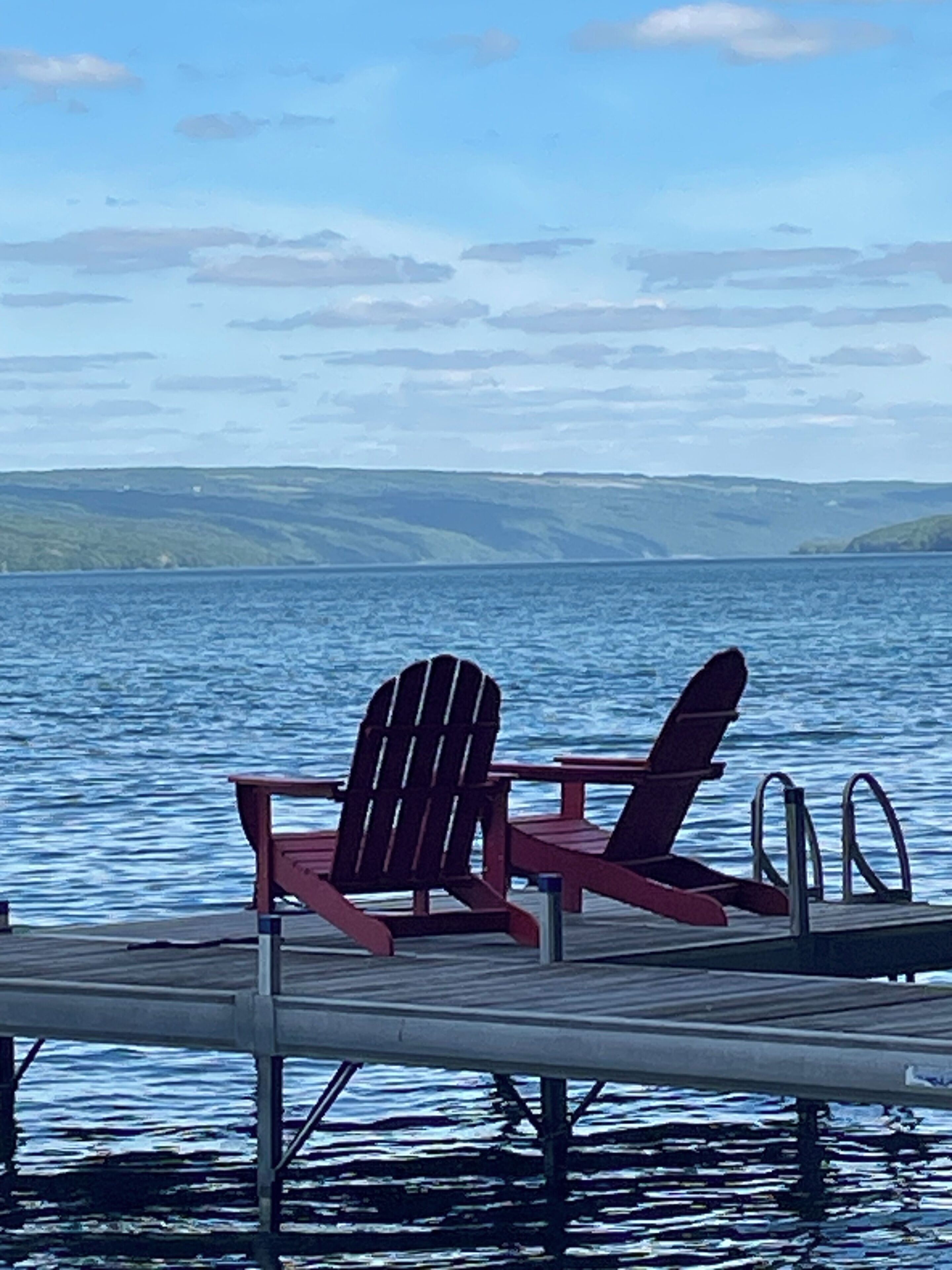 Une jetée en bois avec deux chaises Adirondack donnant sur un lac paisible.
