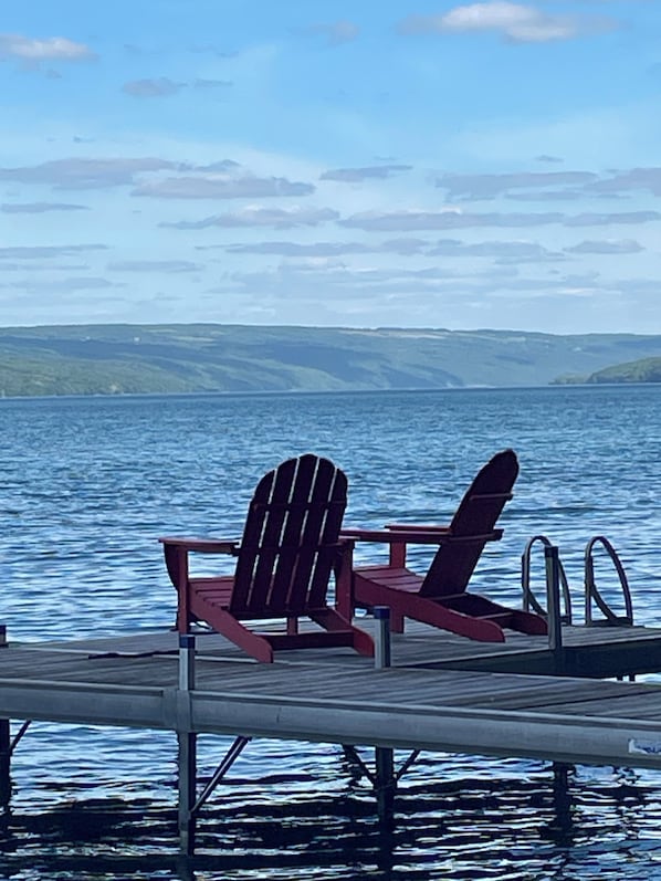 A wooden dock with two Adirondack chairs facing a calm lake.