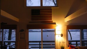 A cozy living room with a large window overlooking a snowy landscape, a fireplace, and a view of the American flag.