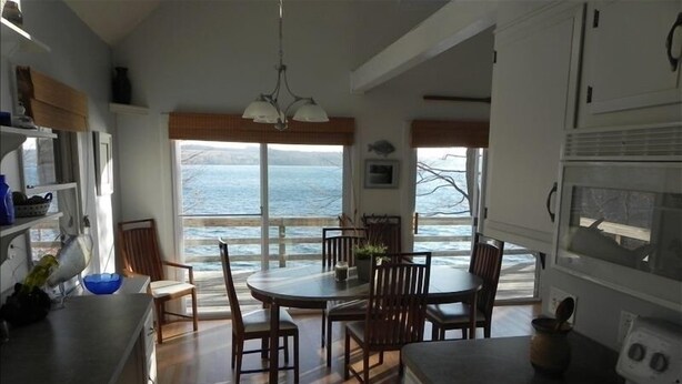 A kitchen with a large window overlooking the ocean, wooden flooring, and a dining area with chairs and a table.