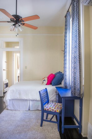 A bedroom with a bed, a desk, a chair, and a ceiling fan.