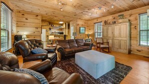 Ein gemütliches Blockhaus-Interieur mit Holzwänden und -decken, Ledermöbeln, einer Essecke und einer Küche.
