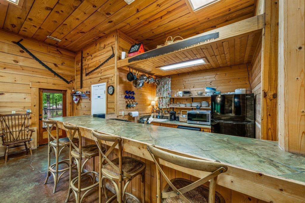 A wooden interior with a bar area, chairs, a refrigerator, and kitchen appliances.