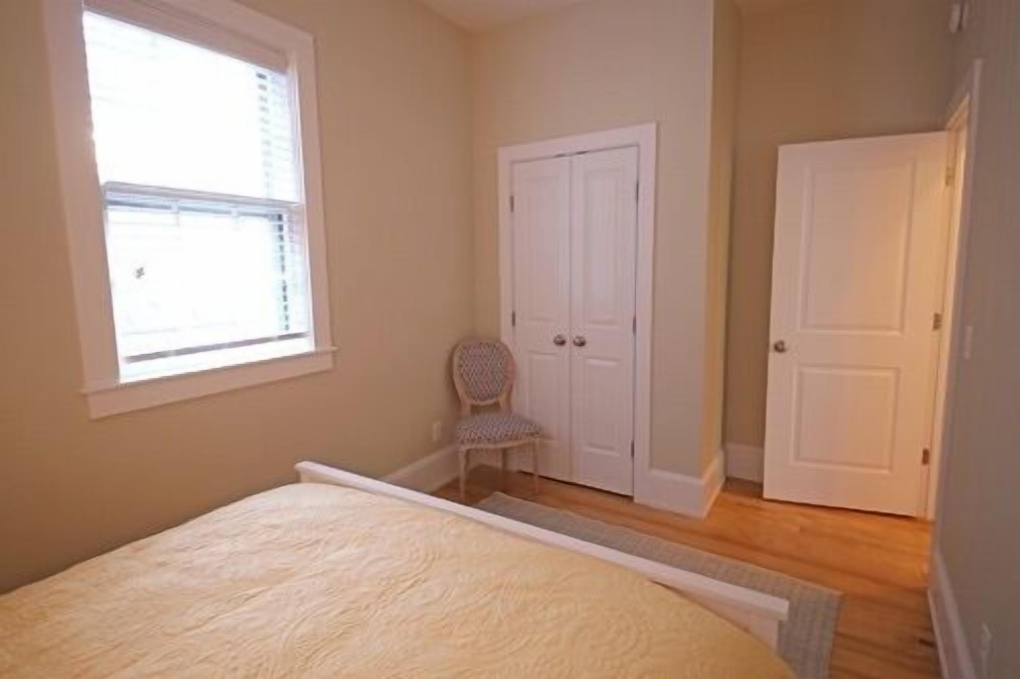 A bedroom with a bed, a chair, and two doors.