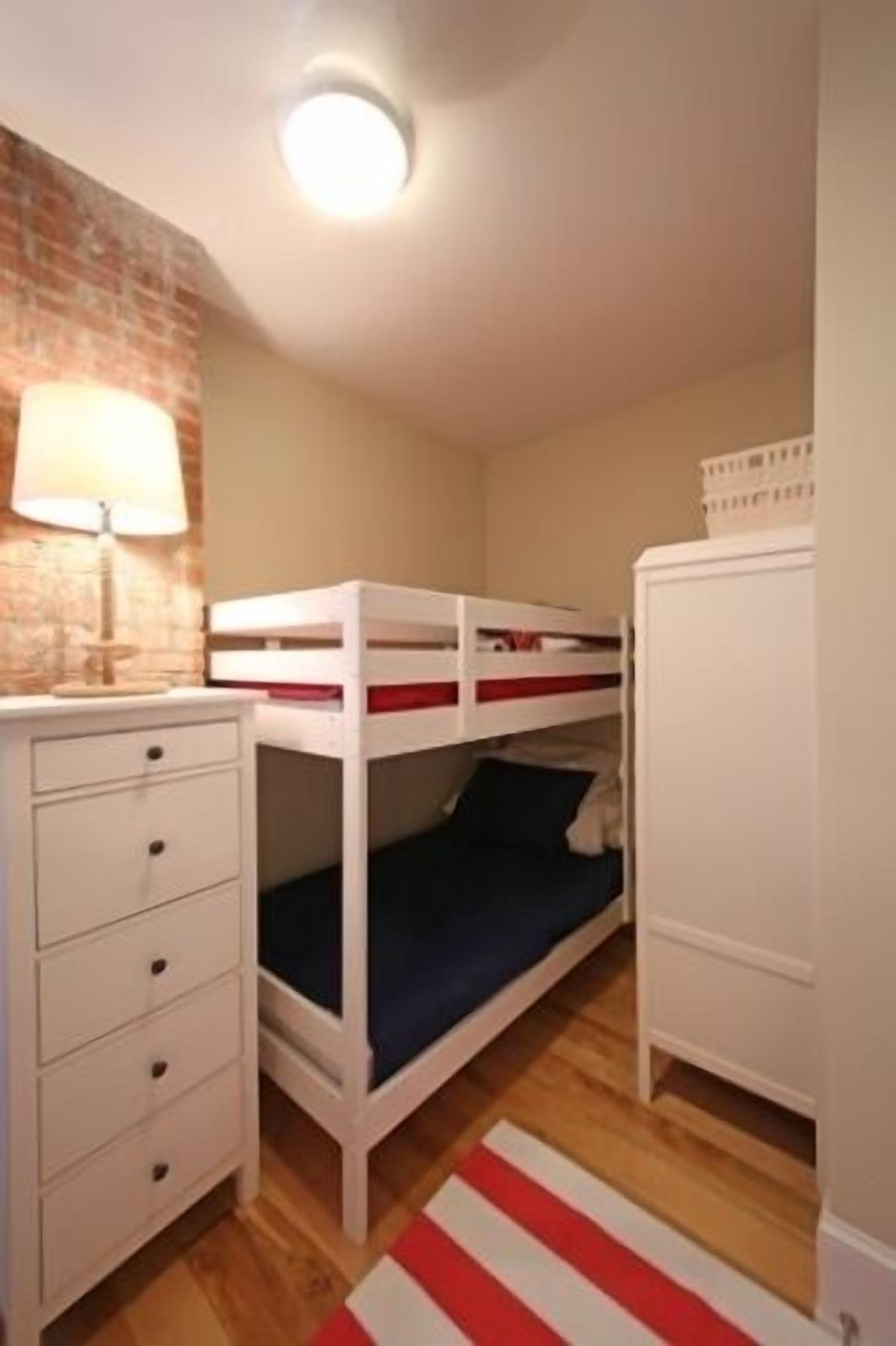 A bunk bed room with a desk and drawers, a lamp, and a wardrobe.