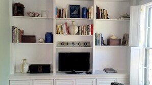 A living room with a white entertainment unit containing books, a television, and a 'Cisco' sign.