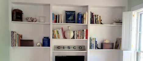 Una sala de estar con un mueble blanco para entretenimiento, estanterías, un televisor y un sillón estampado.