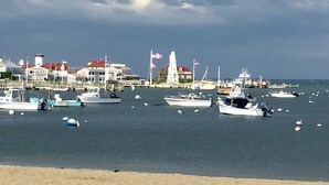 A marina with multiple boats docked, a sandy beach, and buildings in the background.