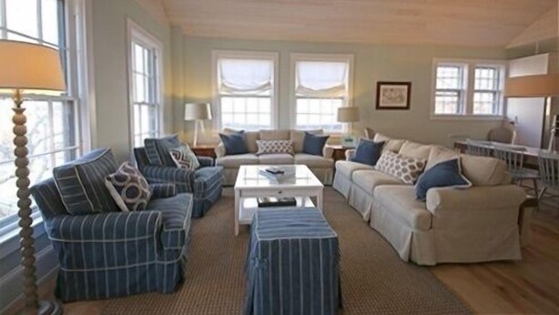 A spacious living room with a large window, a sofa set, a coffee table, and a lamp.