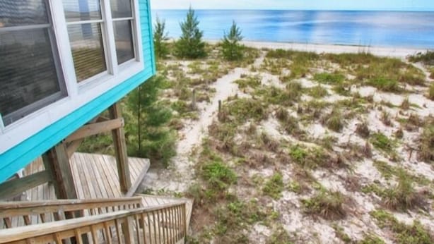 Une propriété située en bord de mer, dotée d’une terrasse en bois et offrant une vue sur l’océan.