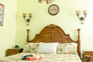Un dormitorio con cabecera de madera, ropa de cama floral, un reloj en la pared y apliques.