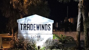 A sign for 'Tradewinds' with a phone number 24568, surrounded by greenery and palm trees at night. - Beautiful Ocean Front Condo in Orange Beach....Affordable Prices (Orange Beach)
