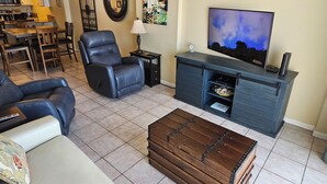 A living room with a leather recliner, a TV, a wooden coffee table, and a kitchen in the background. - Beautiful Ocean Front Condo in Orange Beach....Affordable Prices (Orange Beach)