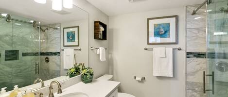 A modern bathroom with a large mirror, a sink with multiple faucets, a toilet, and a glass shower enclosure.