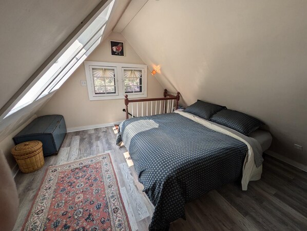 Ein Schlafzimmer mit schrägen Wänden, einem Bett mit gemusterten Betttextilien, einem kleinen Teppich und einer Holzbank.
