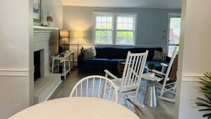 Un salon avec une cheminée, un canapé bleu, un fauteuil à bascule blanc, une petite table et une lampe.