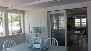 Un espace repas comprenant une table et des chaises, une lampe, et une vue sur l’extérieur grâce à de grandes fenêtres.