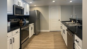A modern kitchen with white cabinetry, stainless steel appliances, and a wooden floor. - Multi-Family, sleeps 12, GULF FRONT with BEACH VIEWS FROM EVERY ROOM (Pensacola Beach)