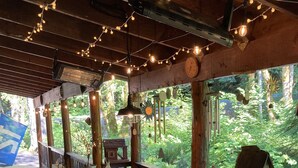A wooden deck with a long table and benches, string lights, and a view of a lush forest. - Pine Lodge - 9 beds;  Extra fees  for 7+ Hot Tub Sauna AC EV Charger Pets (Packwood)